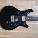 Černá elektrická kytara s tmavým hnedým hmatníkem a černým pickguardem. Nástroj je vybaven dvěma humbuckery, dvěma potenciometry a jedním přepínačem.…