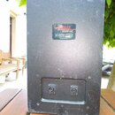 Zadní strana černého, hranatého reproduktoru. Uprostřed je nalepený štítek s nápisy „APOGEE SOUND-INC“, „AE-3 LOUDSPEAKER“ a „MADE IN USA“. V dolní č…