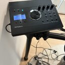 Černý elektronický bicí modul s displejem, na kterém je nápis "KIT 100 User Kit". Na spodní hraně je logo "Roland" a vpravo nápis "DRUM SOUND MODULE…