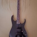 Černá elektrická kytara s tmavým hnedým hmatníkem. Na hlavě je bílý nápis Ibanez. Nástroj má dva humbuckery, jeden ovládací knoflík a přepínač snímač…