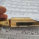Zlatý kovový mouthpiece s nápisem "Pariish" na boční straně. Povrch vykazuje drobné škrábance a známky opotřebení. Předmět je položen na listech s hu…