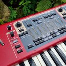 Červený elektronický klavír s bílými a černými klávesami. Horní panel obsahuje množství posuvníků, tlačítek a ovladačů s nápisy jako ORGAN MODEL, ORG…