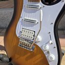 Elektrická kytara s tělem v provedení sunburst a bílým pickguardem. Nástroj má tři snímače typu single-coil, chromovaný most s páčkou a tři bílé ovlá…
