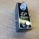 Kytarový efekt pedál v kovovém šedém šasi s černým horním panelem. Na panelu je bílý nápis „EP booster BY xotic usa“ a označení „OUT“ u výstupního ko…
