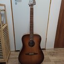 Akustická kytara s korpusem v tmavě hnědém přechodovém odstínu (sunburst) a hnedým hmatníkem. Na hlavě nástroje je viditelné logo Fender. Kytara stoj…