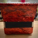 Červená akordeon s povrchem imitujícím mramor nebo masivní plast. Nástroj má černý měch a černé popruhy z kůže. Na povrchu nejsou viditelné žádné zna…