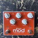 Oranžový efekt pedál v kovovém šasi s bílými oválnými knoflíky. Na spodní části je bílý nápis "dedalo mod" a pod ním text "MODULO LUNAR / PHASER". Ov…