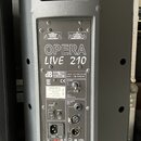 Šedý aktivní reproduktor s plastovým krytem. Na zadním panelu je velký bílý nápis OPERA LIVE 210 a logo db TECHNOLOGIES. Štítek obsahuje text: OPERA…