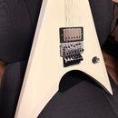 Bílá elektrická kytara s ostrými hranami v tvaru V. Nástroj má jeden humbucker u kobylky, Floyd Rose kobylku a jeden ovládací knoflík. Povrch je hlad…