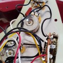 Fotografie zachycuje vnitřní elektroinstalaci hudebního nástroje. Jsou vidět tři kovové potenciometry, několik barevných vodičů (černý, červený, bílý…