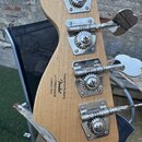 Zadní strana hlavy basové kytary z přírodního dřeva se čtyřmi chromovanými ladicími mechanismy. Na dřevě je černý nápis: Designed and Backed by Fende…