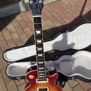 Elektrická kytara typu Les Paul s tělem v červeno-žlutém sunburst provedení. Na hlavě je bílý nápis Gibson a svisle orientovaný nápis Les Paul MODEL.…