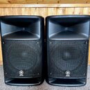 Dva černé reproduktory s mřížkami a hornovými výstupníky v horní části. Na spodní části mřížek je umístěno kulaté logo s nápisem YAMAHA. Povrchy jsou…
