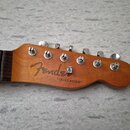 Fotografie zachycuje hlavu dřevěné elektrické kytary v přirozené barvě. Na povrchu je vidět nápis Fender a pod ním v uvozovkách text "TELECASTER". Ná…