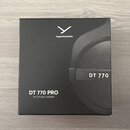 Černá čtvercová krabice s obrázkem sluchátek. Na horní části je bílé logo a nápis beyerdynamic, vpravo je uveden model DT 770. V levém dolním rohu je…