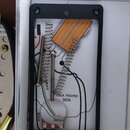Černý obdélníkový rám s otvory pro šrouby, uvnitř kterého jsou položeny dva kovové šrouby a jeden pružinový mechanismus. Pod nimi je vidět schéma s n…