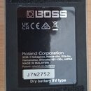 Zadní strana černého efekt pedálu s dvěma černými suchými pásy. Na středovém štítku je bílé logo BOSS a nápis Roland Corporation s adresou v Japonsku…