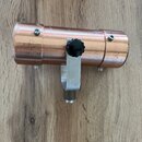 Měděný cylindrický objekt s kovovým držákem a černým plastovým knoflíkem. Povrch je viditelně opotřebovaný s četnými škrábancem a odřeninami. Na před…