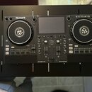 Černý DJ 컨트롤러 s dvěma jogovými koly a centrálním displejem. Na přístroji jsou viditelné nápisy Numark a MIXSTREAM PRO oraz logo engine os v dolní čás…
