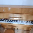 Světle hnědé pianino s lakovaným dřevěným povrchem. Na krytu nad klávesnicí je viditelný nápis "SMILE". Nástroj vykazuje známky opotřebení v podobě š…