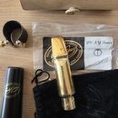 Zlatý kovový munční nástroj (mouthpiece) s nápisem Jody Jazz na spodní části. Vedle něj je černý ligaturen z kůže a černé pouzdro s logem Jody Jazz.…