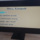 Fotografie zachycuje obrazovku počítačového monitoru s černým rámem. Na displeji je zobrazen text na béžovém pozadí s nadpisem „Blues, Katapult“. Pod…