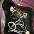 Fotografie zachycuje vnitřní dutinu tmavě červeného trupu elektrické kytary. Uvnitř jsou vidět rozpojené potenciometry a zapletené šedé a černé vodič…