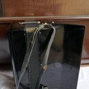 Černý akordeon s lesklým povrchem. Nástroj má černé popruhy, které vykazují známky opotřebení a odloučení materiálu v horní části. Na těle nástroje n…