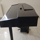 Černý digitální piano v moderním designu s zakryvatelnou klaviatura. Povrch je matný, v horní části se nachází úzký otvor a plochý panel. Nástroj sto…