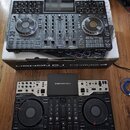 Fotografie zobrazuje dva černé DJ kontroléry značky DENON DJ, model PRIME 4. Horní jednotka stojí na kartónové krabici s nápisem DENON DJ PRIME 4 a v…