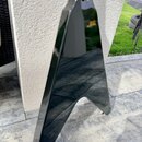 Detailní pohled na spodní část korpusu černé elektrické kytary s ostrými hranami. Povrch je vysoce lesklý a zrcadlí okolí, v horní části je viditelný…