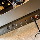 Detail zadní strany černého elektronického zařízení s několika konektory. Jsou zde viditelné nápisy MIDI IN, MIDI OUT, PEDAL A, PEDAL B a USB, dále n…