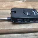 Černý oválný kontrolér s připojeným kabelem a konektorem typu jack. Na horní straně je umístěn kulatý ovratový knoflík a nápisy Fender MUSTANG MICRO.…