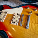 Detail elektrické kytary s žlutě-červeným přechodem barvy (sunburst) a výraznou strukturou dřeva. Nástroj má dva krémové snímače, bílý pickguard a čt…