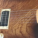 Detail elektrické kytary s hnědým dřevěným povrchem a javorovým hmatníkem. Na snímači je viditelný nápis Seymour Duncan. Kytara má chromovaný most a…
