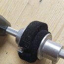 Detailní záběr na kovový držák mikrofonu s černým plastovým kloubem a stahovacím šroubem. Na držáku je nasazený černý, měkký plišový nebo pěnový krou…