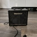 Černý kytarový kombo zesilovač s rukojetí nahoře a černou síťovkou. Na přední straně je bílý nápis Blackstar®. Z přístroje vede napájecí kabel s vidl…