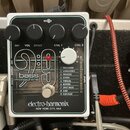 Bílý efekt pedál s černým předním panelem a nápisem bass machine 9:9. Na spodní části je logo electro-harmonix NEW YORK CITY, USA. V horní části jsou…