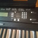 Černý digitální klavír s bílými a černými klávesami. Na panelu je viditelné logo YAMAHA a označení modelu EZ-220. Nástroj obsahuje displej, numericko…