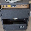 Zadní strana černého kytarového zesilovače s kovovými rohy. Na horním zlatavém panelu jsou vidět konektory a nápisy: PRODUCT OF JBL, R/L, SLAVE ON SL…