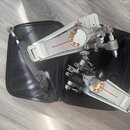 Dvě pedály bicích pedálů v černé přepravní tašce. Pedály jsou vyrobeny z kovového materiálu stříbrné barvy s oranžovými detaily a mají na sobě nápis…