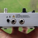 Stříbrné kovové zařízení s dvěma zapadacími konektory a přepínačem. Na povrchu je nápis „ATTENTION: DO NOT CONNECT CABLOADER TO YOUR AMPLIFIERS SPEAK…