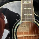 Černá akustická kytara s hnědým hmatníkem a perleťovými vložkami. Uvnitř ozvučnice je vidět štítek s nápisy Ibanez, MODEL No. AEL30E-BK-27 a SERIAL N…