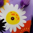Detail efekt pedálu s fialovým povrchem a barevnými květinovými motivy. Na horní části jsou vidět dvě fialové plastové voliče a nápisy C a V. Uprostř…