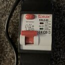 Elektrický jistič v černém plastovém krytu s bílým předním panelem. Na panelu je červené tlačítko označené písmenem T a červený přepínač s nápisem I-…