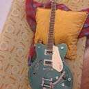 Polodupatá elektrická kytara v tyrkysové barvě s bílým bindingem a krčkem z tmavého dřeva. Na hlavě je nápis Gretsch, na pickguardu je logo GRETSCH a…