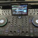 Černý DJ 컨트롤러 Denon DJ PRIME 4+. V horní části je umístěn velký barevný displej s rozhraním softwaru. Nástroj má dva osvětlené jog-wheels, faderové p…