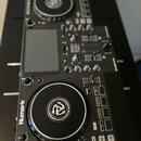 Černý DJ 컨트롤러 s dvěma jogovými koly a centrálním míchacím sekcí. Na levé straně je svisle napsaný bílý nápis Numark. Na ovládacích prvcích jsou vidit…