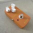 Oranžový kytarový efekt s bílými oválovými knoflíky. Na horní straně jsou nápisy Volume, Focus, Sweet Baby, Overdrive, OUT, 9V DC a TRUE BYPASS, v pr…