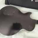Zadní strana elektrické kytary v tmavě hnědé nebo černé barvě s lesklým povrchem. Na těle jsou dva černé plastové kryty připevněné šroubky, jeden obd…